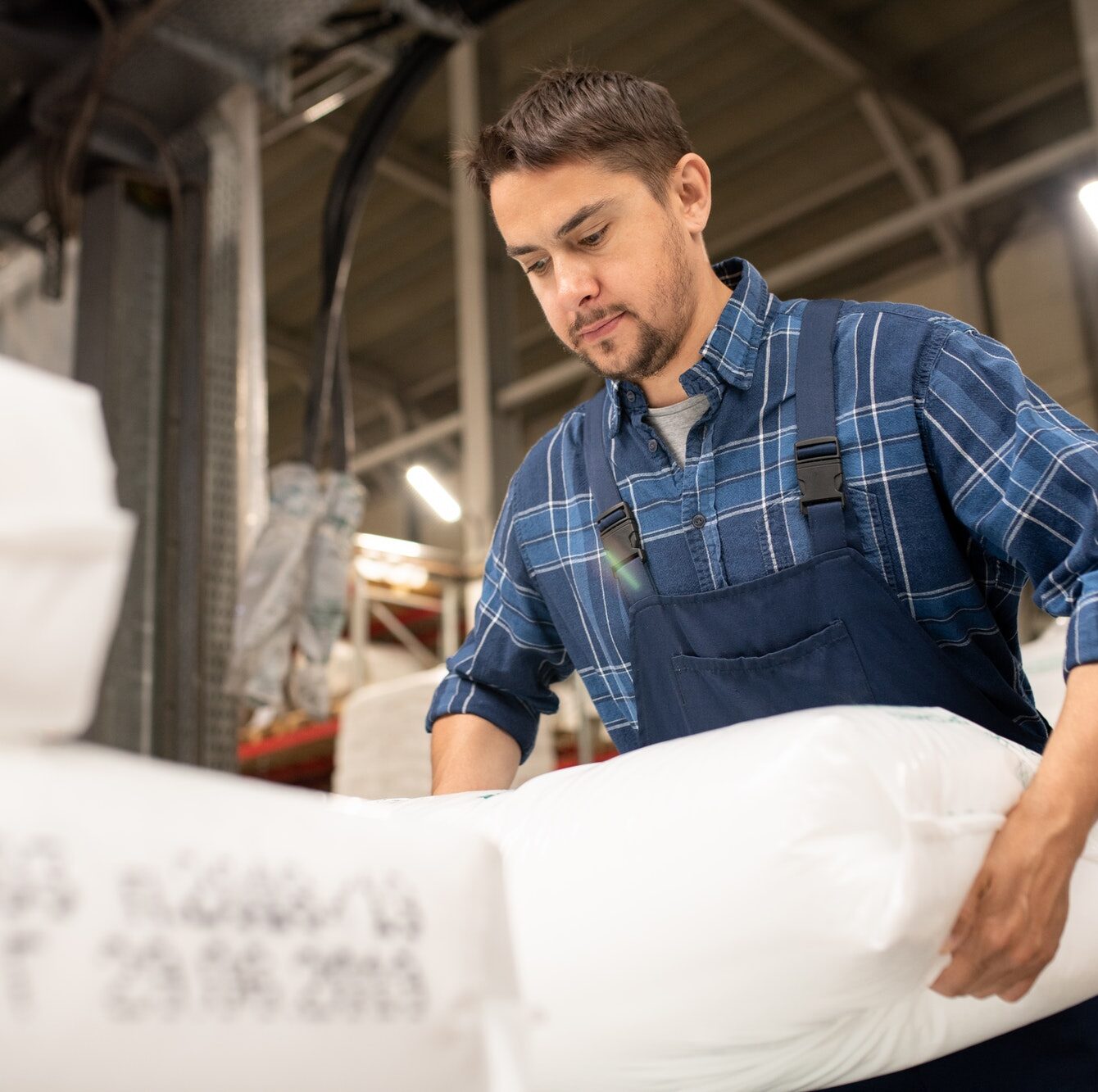 Young worker of polymer production factory loading sacks with plastic granules